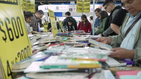 Low-Angle-Ansicht-Von-Menschen,-Die-Auf-Der-Buchmesse-In-Buenos-Aires-Durch-Einen-Stapel-Bücher-Blättern