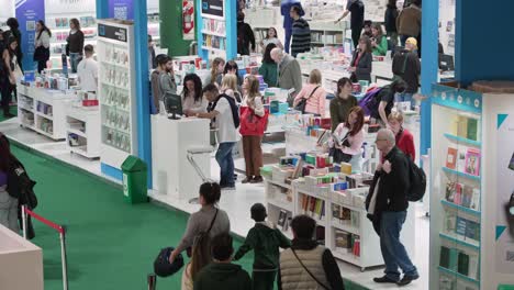 Blick-Von-Oben-Auf-Weiße-Und-Blaue-Bücherregale-Auf-Der-Buchmesse,-Während-Leute-Vorbeigehen