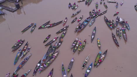 Boats-from-floating-food-market-on-Sungai-Martapura-river-in-Indonesia-during-cloudy-day,-aerial