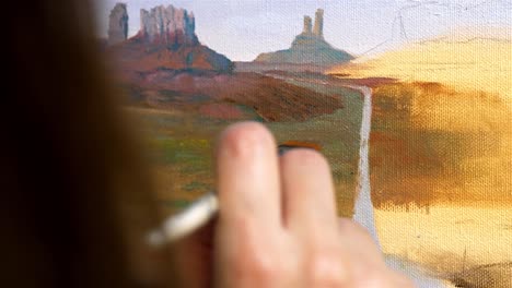 Medium-closeup-of-artists-using-wide-tip-brush-to-add-desert-texture-to-oil-painting-of-monument-valley