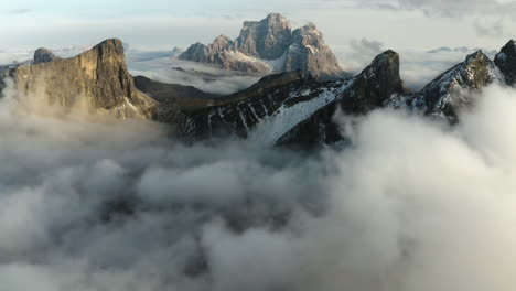 Aerial-view-tilting-over-mist,-toward-rocky-limestone-peaks,-sunrise-in-Tyrol,-Italy
