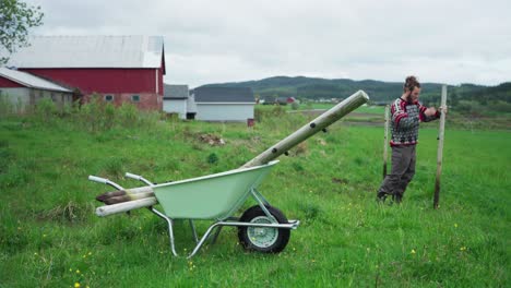 Man-In-Countryside-Removing-Fence-Pole-And-Placed-Into-Wheelbarrow