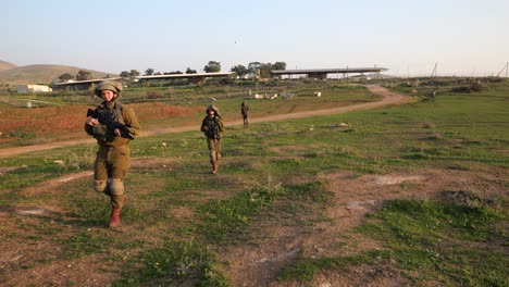 Military-man-with-gun-picking-up-object-from-the-ground-while-walking