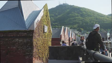 Tourist-Resting-On-Pipe-Railing-Outside-Bay-Hakodate-Beside-Kanemori-Red-Brick-Warehouses