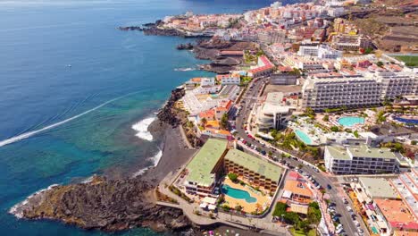 Aerial-morning-view-of-Tenerife-Santiago-Del-Teide-La-Arena-of-Spain-with-the-blue-water-and-a-boat-in-the-sea-and-buildings-on-the-other-side