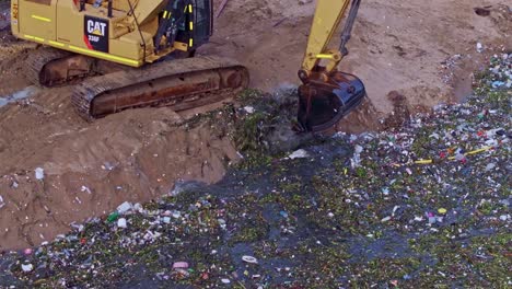 Excavator-digs-out-trash-from-a-sand-beach,-concept-of-environment-pollution