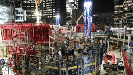 Night-sight-of-skyscraper-construction-site-with-cranes-and-scaffolding,-wide-panning-shot