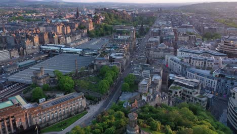 Edinburgh-city-center-train-station-drone-aerial-cityscape-view-at-golden-hour,-lowering,-Scotland