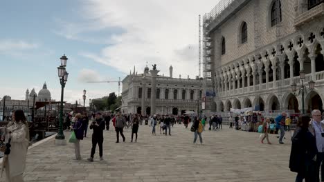 Touristen,-Die-Um-Den-Pier-Neben-Dem-Dogenpalast-Herumlaufen,-Mit-Der-Biblioteca-Nazionale-Marciana-Im-Hintergrund
