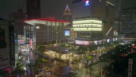 Toma-Aérea-De-Luces-Intermitentes-En-El-Centro-De-La-Ciudad-De-Taipei-Por-La-Noche-Durante-El-Día-Lluvioso---Automóviles-Pasando-Por-Un-Cruce-En-Una-Metrópolis-Asiática