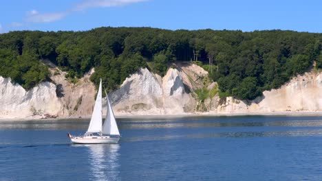 The-very-famous-chalk-cliffs-of-the-Rügen-Island-in-Germany,-viewed-from-the-baltic-sea,-with-a-small-passing-sailboat