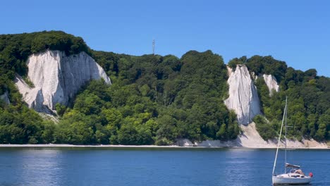 The-very-famous-chalk-cliffs-of-the-Rügen-Island-in-Germany-with-the-Königsstuhl-vantage-point,-viewed-from-the-baltic-sea,-with-a-small-passing-sailboat
