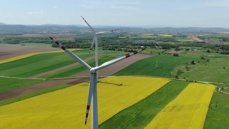 Static-aerial-view-of-wind-turbine-blades-spinning-above-rapeseed-farm-field