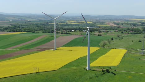 Aerial-orbit-around-windmill-turbines-at-wind-farm-above-yellow-blooming-fields