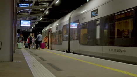 Familia-Tomando-El-Tren-Con-Equipaje-En-La-Plataforma-De-La-Estación-De-Tren-De-La-Terminal-Del-Aeropuerto-De-Gdansk-Por-La-Noche