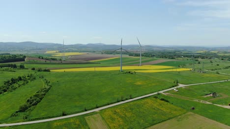 Panoramic-aerial-static-view-of-wind-farm-turbines-spinning-large-blades,-blue-sky