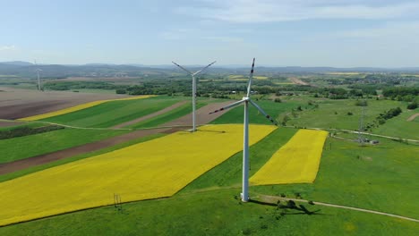 Aerial-orbit-around-two-windmill-turbines-at-wind-farm-in-poland-above-yellow-fields