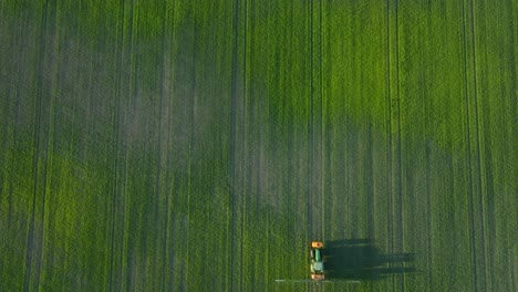 Aerial-establishing-view-of-a-farmer-spraying-crop-fields-with-tractor,-pesticide-and-fertilizer-spraying,-sunny-summer-evening,-golden-hour-light,-wide-descending-drone-birdseye-shot