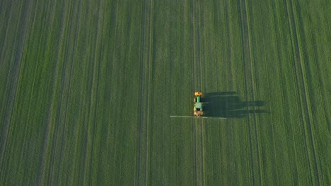 Aerial-establishing-view-of-a-farmer-spraying-crop-fields-with-tractor,-pesticide-and-fertilizer-spraying,-sunny-summer-evening,-golden-hour-light,-wide-birdseye-drone-shot-moving-forward