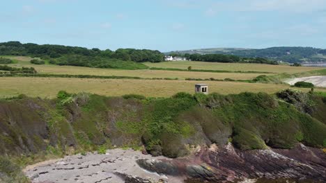 Traeth-Lligwy-Anglesey-eroded-coastal-shoreline-aerial-view-reverse-dolly-across-scenic-green-rolling-Welsh-weathered-coastline