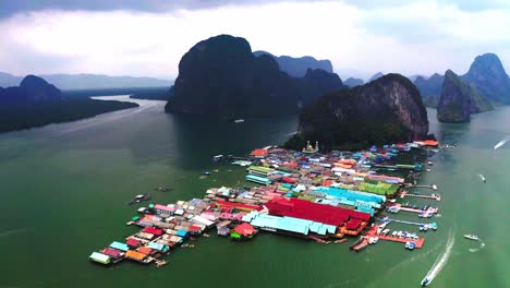 Vista-Aérea-Del-Pueblo-Flotante-De-Panyee-En-La-Que-La-Cámara-Del-Dron-Avanza-Y-Las-Casas-Flotantes-Son-Visibles-En-El-Agua-Detrás-De-Las-Hermosas-Y-Sorprendentes-Montañas-En-Medio-Del-Mar.