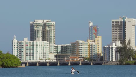 Persona-Kayaks-En-Aguas-Abiertas-Con-Los-Hoteles-Hilton-Y-El-Puente-Dos-Hermanos-Del-área-Del-Condado-De-La-Ciudad-Al-Fondo---Panorámica-Hacia-La-Derecha