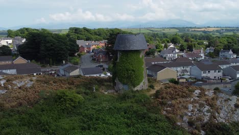 Melin-Wynt-Y-Craig-Stillgelegte-Llangefni-Windmühle,-Mit-Efeu-Bedeckter-Hügel,-Wahrzeichen,-Luftaufnahme-Mit-Blick-Auf-Walisische-Nachbarschaftswohnungen