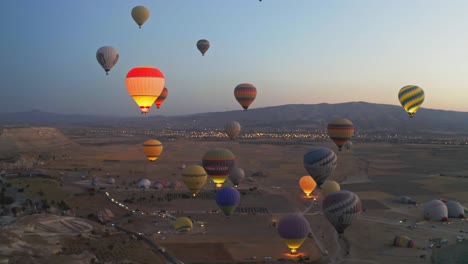 Standardaufnahme-Der-Türkei,-Drohne-Aus-Der-Luft-Folgt-Vielen-In-Der-Luft-Fliegenden-Ballons-Und-Menschen,-Die-Im-Ballon-Reisen-Und-Den-Sonnenuntergang-Und-Das-Licht-Des-Ballons-Genießen