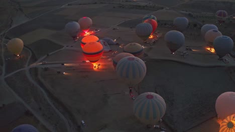 established-shot-in-which-the-camera-is-panning-in-a-valley-in-Cappadocia,-Turkey,-many-hot-air-balloons-are-getting-ready-to-take-off-and-there-are-flames,-Colorful-hot-air-balloon-festival-floating