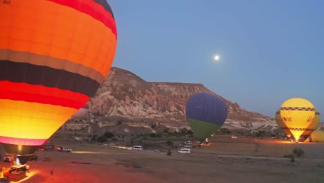 Night-scene-with-aerial-drone-camera-moving-in-front-of-a-valley-in-Cappadocia-Turkey-with-a-large-number-of-colorful-hot-air-balloons-preparing-to-fly-with-a-large