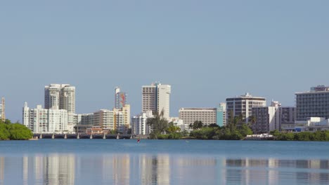 Person-kayaks-in-open-water-with-Hilton-hotels-and-Puente-Dos-Hermanos-of-the-Condado-area-of-the-city-in-the-background---Wide-Shot