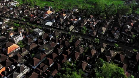 An-aerial-drone-camera-is-flying-over-a-village-in-Ubud-Bali-where-there-are-many-residential-houses-in-brown-color-and-many-vehicles-are-passing-through-the-middle-of-the-road