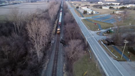 Long-cargo-train-passing-small-town-in-USA,-aerial-drone-front-view
