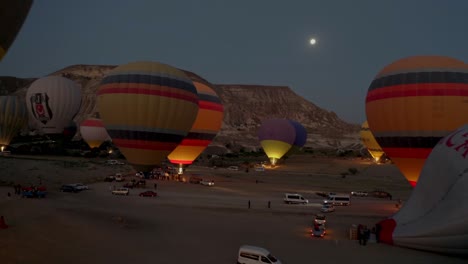 Eine-Luftdrohnenkamera-Zoomt-über-Ein-Tal-In-Kappadokien,-Türkei,-Wo-Sich-Viele-Bunte-Heißluftballons-Auf-Den-Start-Vorbereiten-Und-Die-Insassen-Dies-Ausnutzen