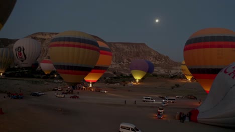 La-Cámara-Aérea-De-Un-Dron-Se-Acerca-A-Un-Valle-En-Capadocia,-Turquía,-Donde-Muchos-Coloridos-Globos-Aerostáticos-Se-Están-Preparando-Para-Despegar-Y-Los-Ocupantes-Están-Aprovechando