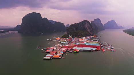 Panyee-floating-village-aerial-view-in-which-the-entire-floating-village-is-visible-from-the-aerial-drone,-which-has-a-rotating-core-forest-with-a-sea-in-between-and-large-sized-mountains-behind