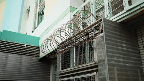 Alambre-De-Púas-Enrollado-Cuelga-De-Ventilación-Metálica-En-Un-Edificio-Industrial-En-Hong-Kong,-Asia