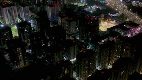 Aerial-camera-moving-forward-above-Surat-cityscape,-high-rise-and-low-rise-building-at-night,-vehicle-passing-on-road-at-night
