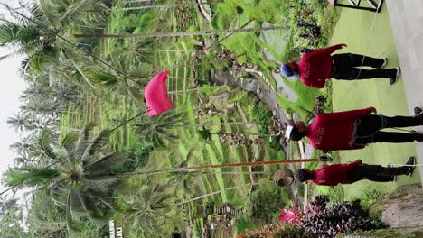 Behind-the-scenes-of-a-girl-in-a-long-red-train-dress-getting-a-photo-shoot-riding-a-swing-with-a-view-to-palm-tree-forest-and-rice-field-terraces-in-Alas-Harum,-Ubud-Bali