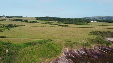 Traeth-Lligwy-Anglesey-eroded-coastal-shoreline-aerial-panning-view-across-scenic-green-rolling-Welsh-countryside
