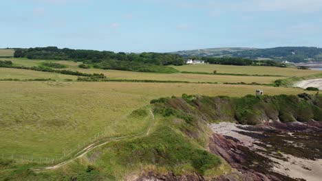 Traeth-Lligwy-Anglesey-eroded-coastal-shoreline-establishing-aerial-view-over-scenic-green-rolling-Welsh-weathered-coastline