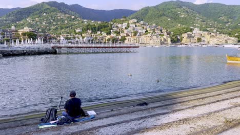 Un-Hombre-Sentado-En-El-Puerto-Deportivo-De-Rapallo-Y-Pescando-En-Una-Tarde-Soleada,-Liguria,-Italia