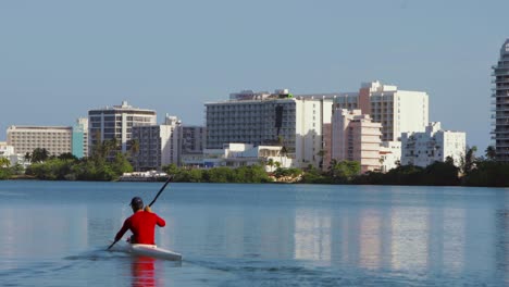 Person-kayaks-in-Condado-Lagoon-with-Hilton-hotels-and-Puente-Dos-Hermanos-in-the-background---Pan-left