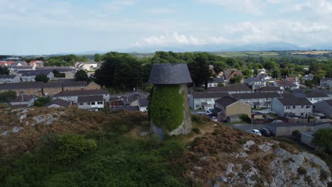 Melin-Wynt-Y-Craig-Llangefni-ivy-covered-hillside-windmill-landmark-aerial-view-overlooking-Welsh-Snowdonia-mountains,-Anglesey
