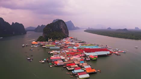 Vista-Aérea-Del-Pueblo-Flotante-De-Panyee-En-La-Que-Todo-El-Pueblo-Flotando-En-El-Agua-Se-Ve-Colorido,-Hay-Una-Montaña-De-Gran-Tamaño-Al-Fondo,-Hay-Un-Bosque-Central-Giratorio-De-Mezquita