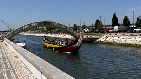 Group-of-tourist-in-gondola-boat-on-channel-in-Aveiro-during-sunny-day,-Portugal---slow-motion-tracking-shot