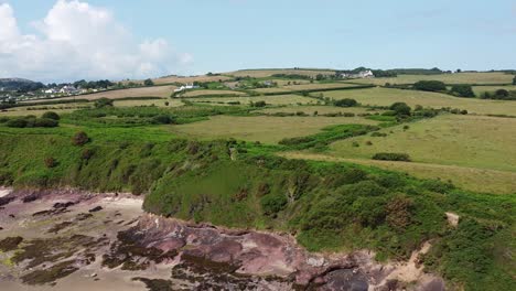 Traeth-Lligwy-Anglesey-eroded-coastal-shoreline-aerial-view-across-scenic-green-rolling-Welsh-weathered-farmland-countryside