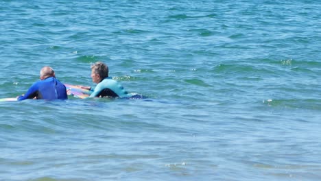 Healthy-active-seniors-paddle-boarding-and-chatting-together-on-turquoise-welsh-waves
