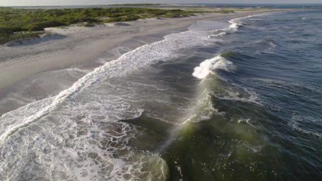 Panning-drone-shot-over-waves-and-surf-crashing-on-beach,-only-a-few-feet-above-water