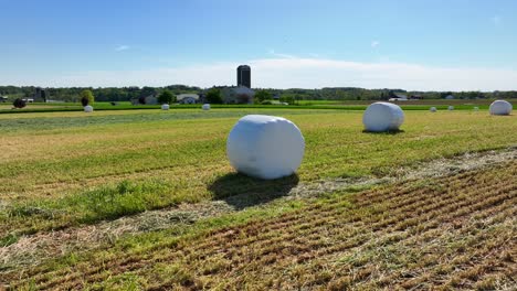 Aerial-orbiting-shot-of-hay-bales-wrapped-in-plastic-foil-on-countryside-field-in-farmland-during-sunny-day